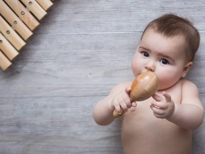 Bebé tumbado jugando con una maraca de madera junto a un xilófono