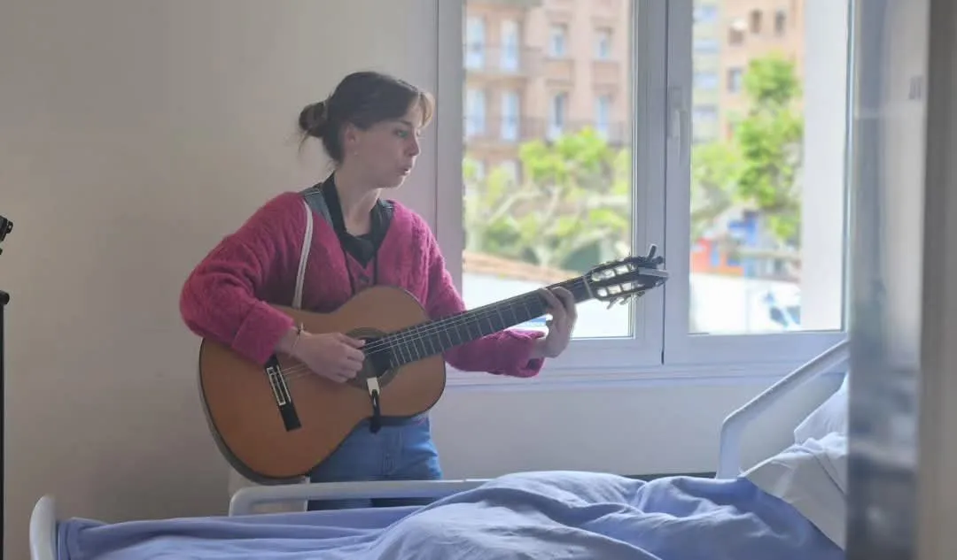 Musicoterapeuta de Concertino tocando la guitarra junto a la cama de un paciente en el hospital