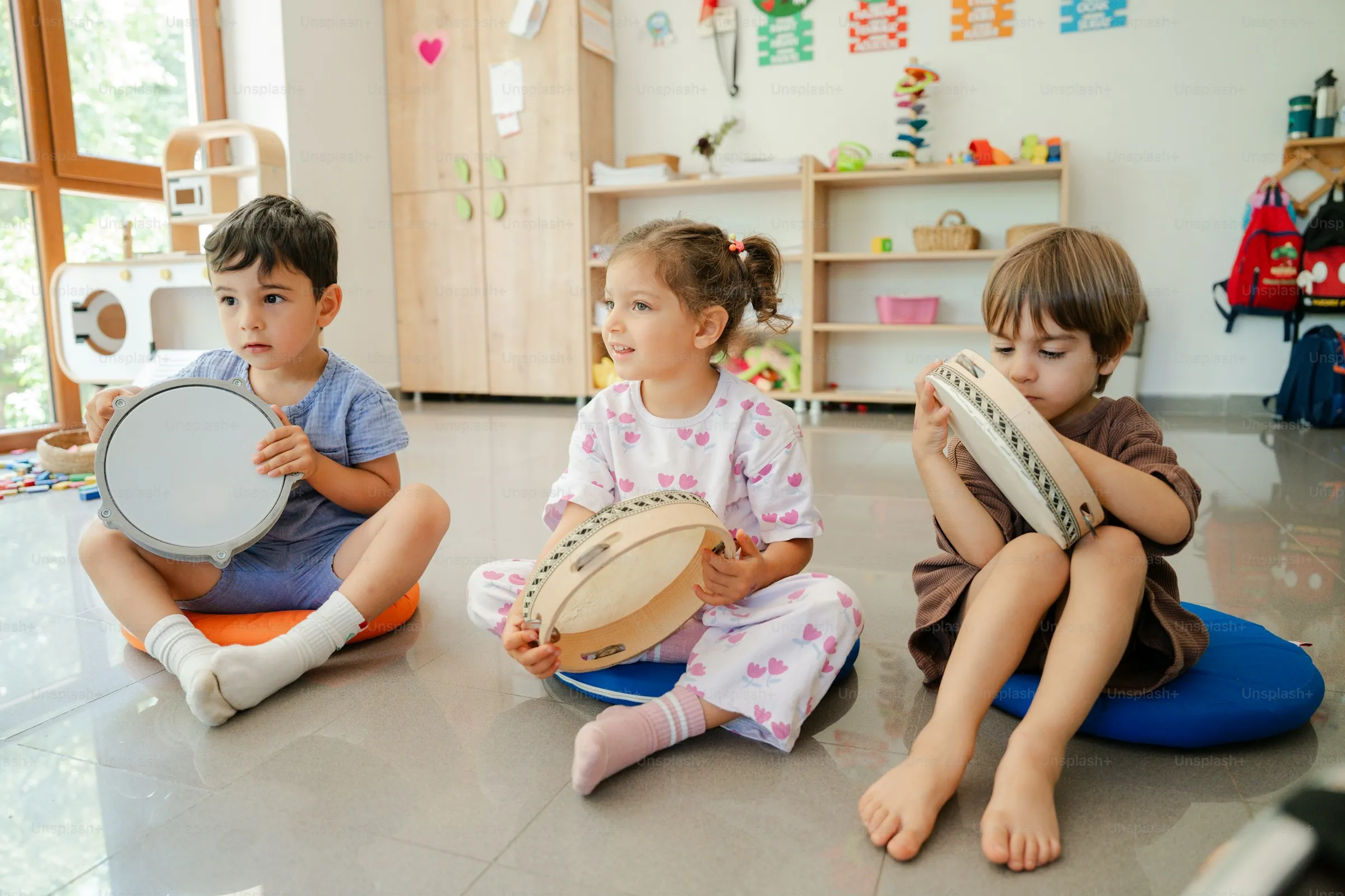 Tres niños sentados en cojines tocando panderos en un aula